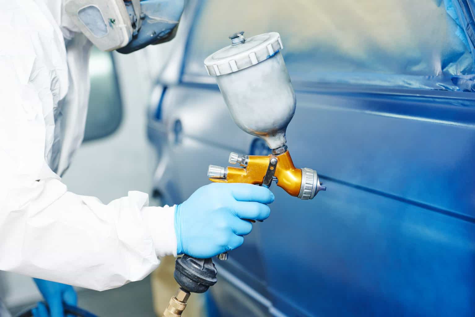painting auto car automobile repairman painter hand in protective glove with airbrush pulverizer painting car body in paint chamber