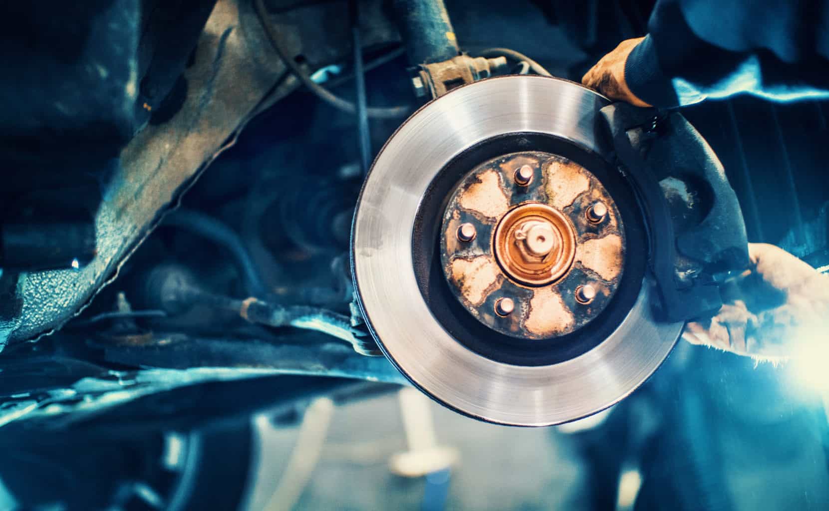 Car service procedure. Closeup of unrecognizable mechanic replacing car brake pads. The car is lifted with hydraulic jack at eye level.